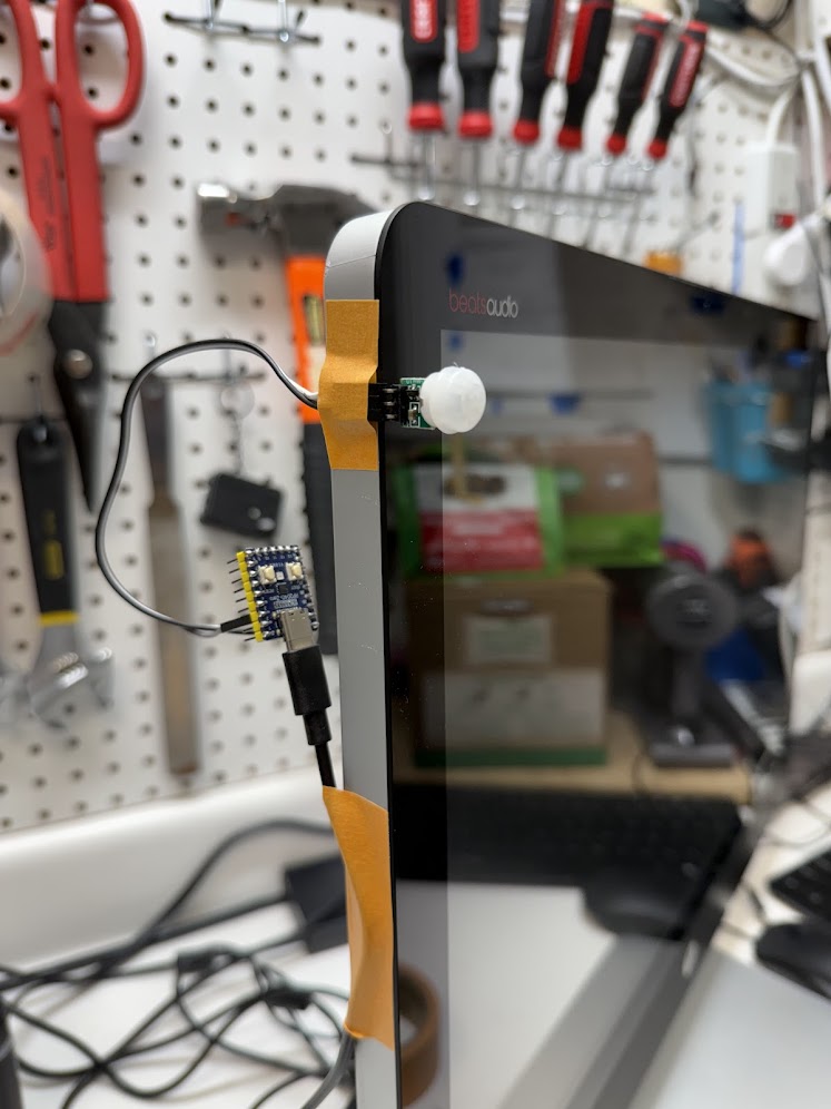 Early MOTIONSENSR prototype — RP2040-Zero and AM312 PIR sensor wired with jumper wires and taped to a living room all-in-one PC
